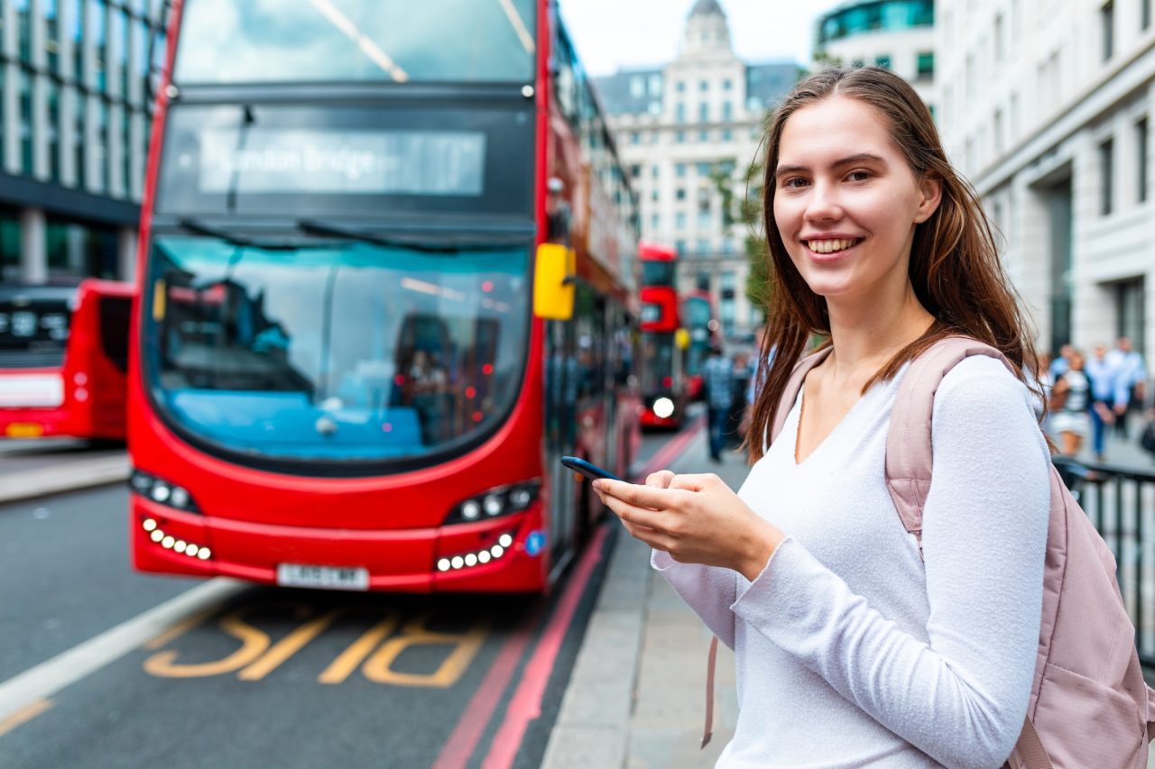 smiling-woman-with-smartphone-at-bus-stop-in-london.jpg